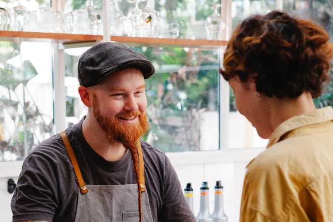 Cheerful hipster barista talking to colleague with coffee at counter - Is he in love with me